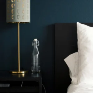 Modern hotel guestroom with moody navy walls, minimalist nightstand, and gold-accented bedside lamp